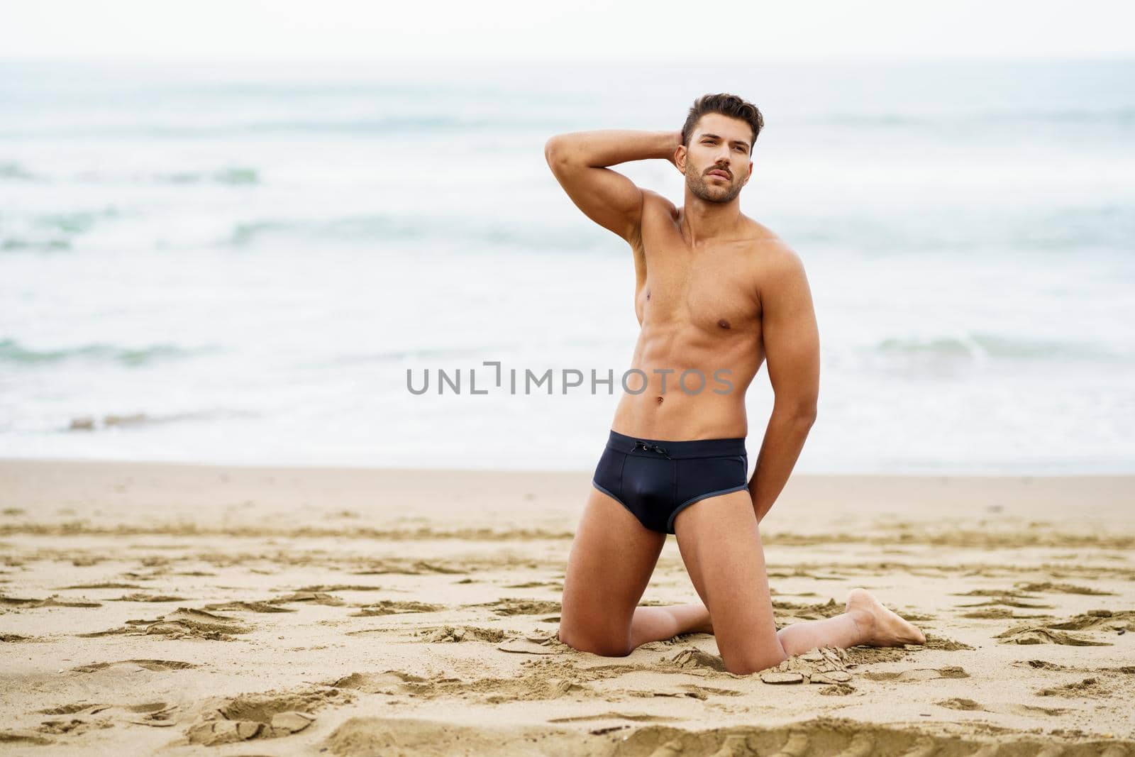 Handsome muscular man on his knees on the sand of the beach