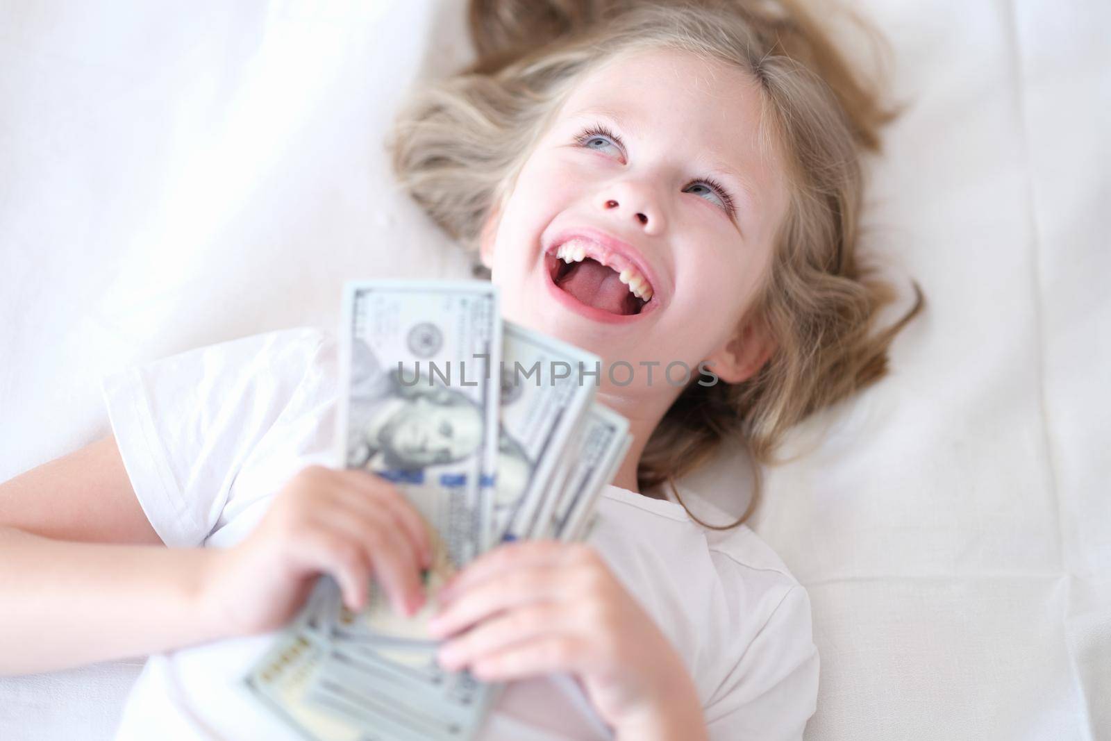 Little girl without front teeth holding money in her hands and smiling. Investment in pediatric dentistry concept