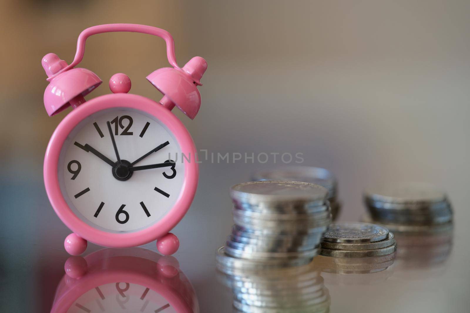 Pink alarm clock standing near pile of coins closeup. Time to make money concept