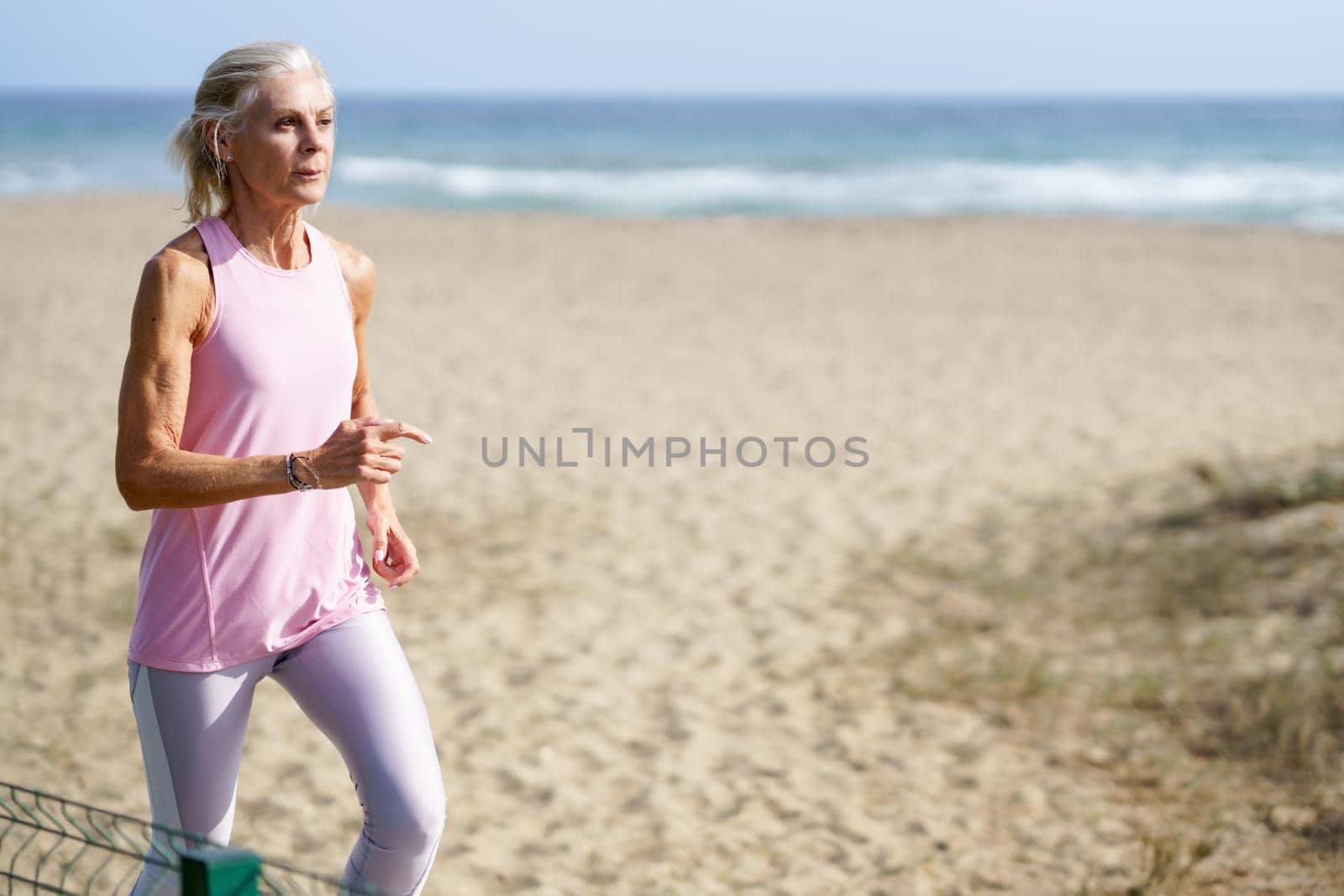 Mature woman running along the shore of the beach. Older female doing sport to keep fit. Concept of healthy living in the elderly. Senior woman in fitness clothing running along beach