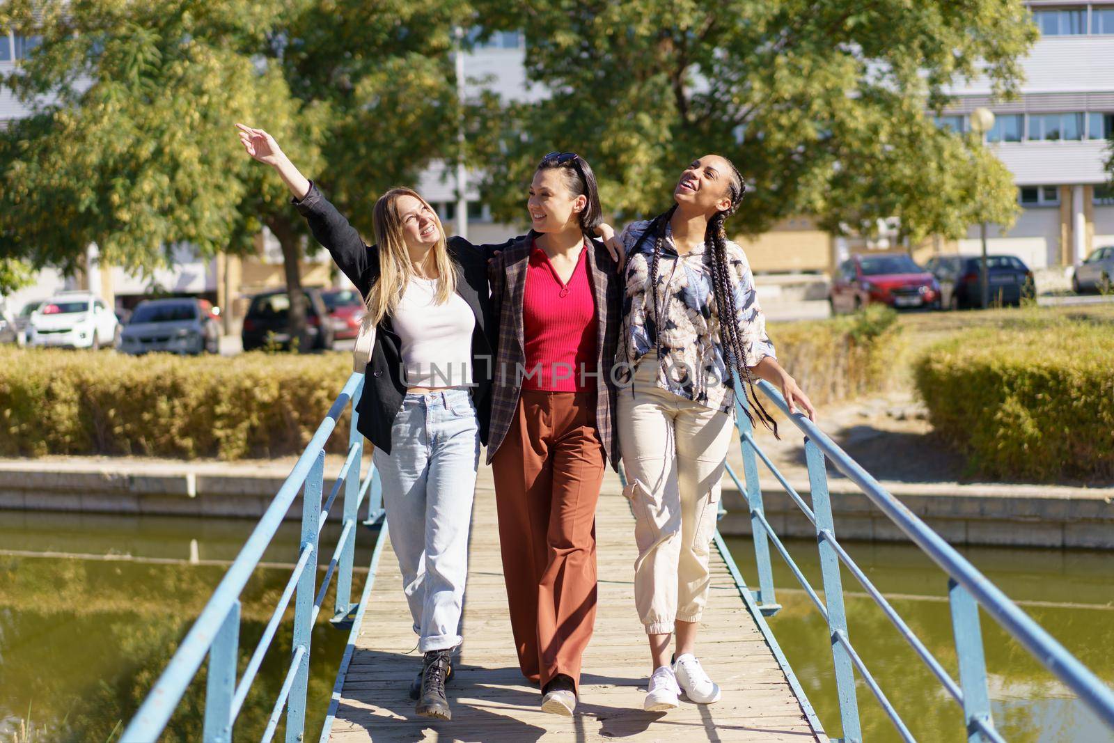 Positive diverse women walking on footbridge by javiindy