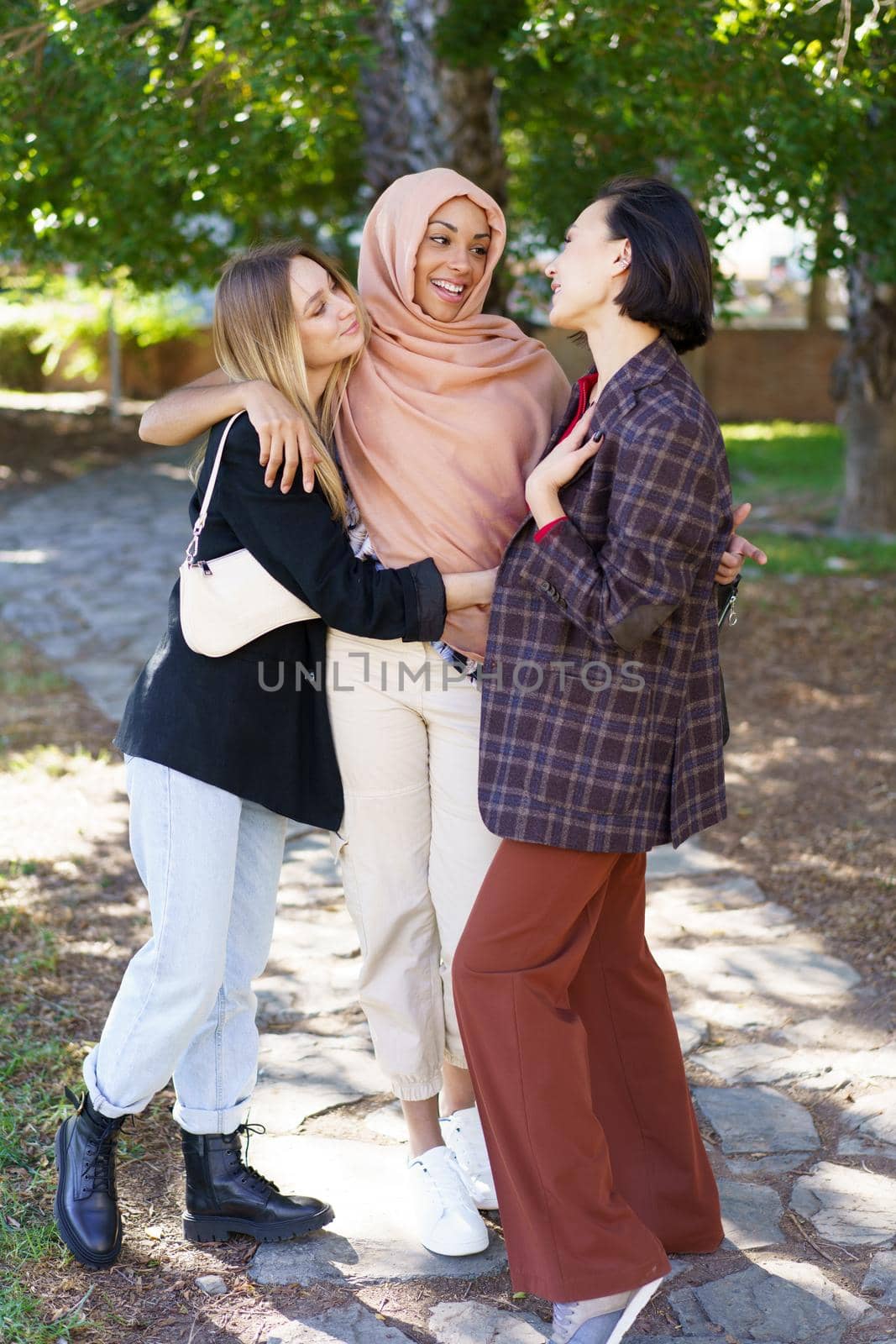 Delighted young diverse women embracing and smiling in park by javiindy