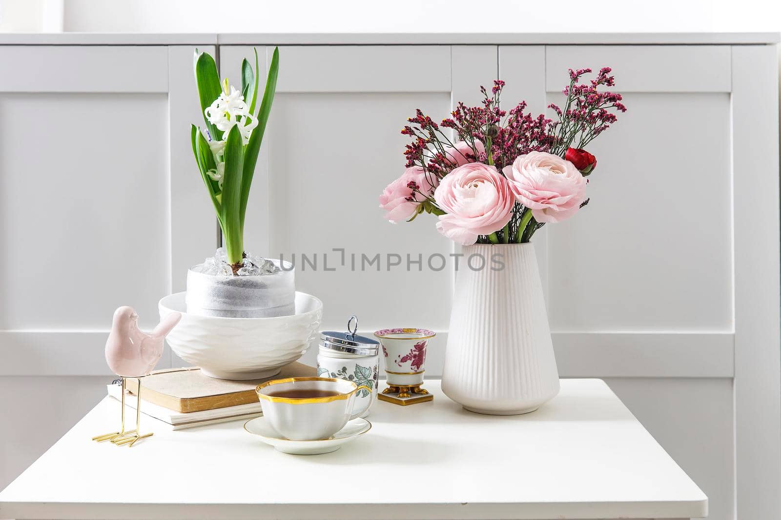 Bouquet of pink Persian buttercups on a white table in front of a chest of drawers. Scandinavian style. Place for text by elenarostunova