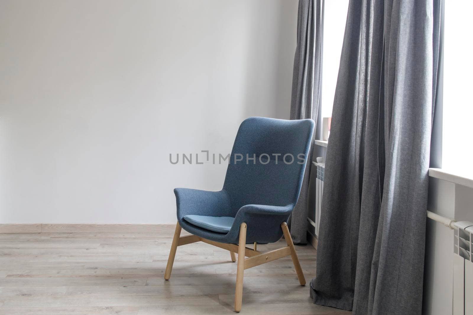 Room interior in Scandinavian style, in white and gray tones. A gray armchair with wooden legs by the window. by elenarostunova