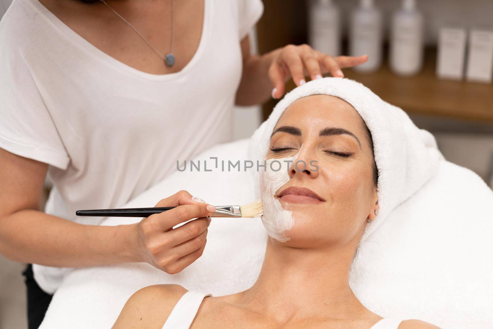 Aesthetics applying a mask to the face of a Middle-aged woman in modern wellness center. by javiindy