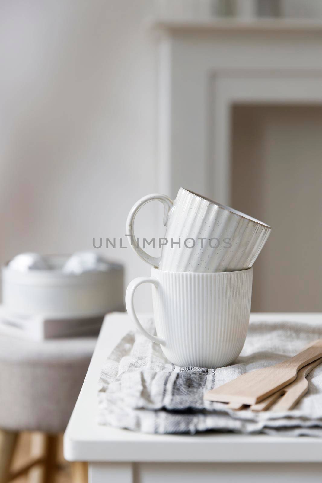 Two white mugs, a kitchen towel, a napkin and wooden frying utensils on the table. Defocus.