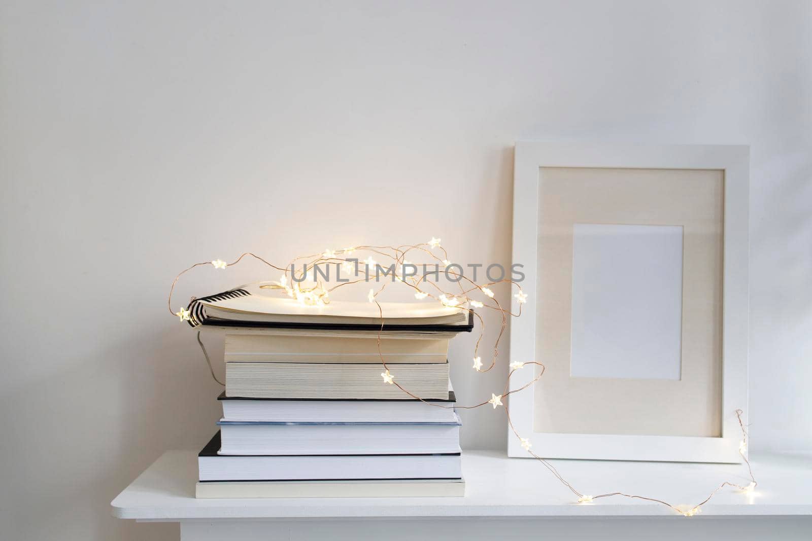 Scandinavian style room interior in white tones. A stack of books, a photo frame, a garland on a wooden surface of a shelf. Copy space.