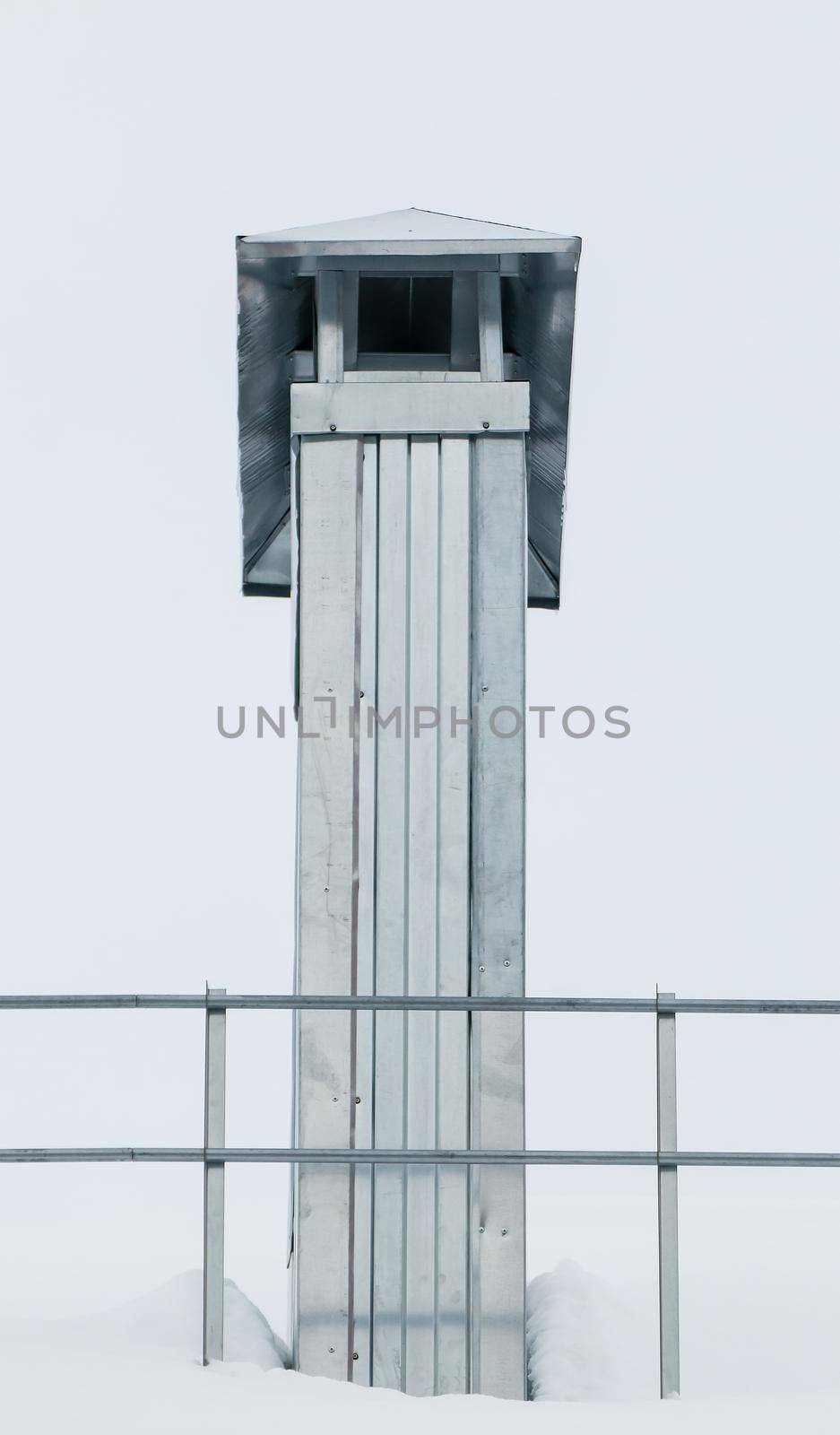 Rectangular metal chimney on the roof of the house. There is white snow on the surface. Against the background of a gray sky. Cloudy winter day, soft light.