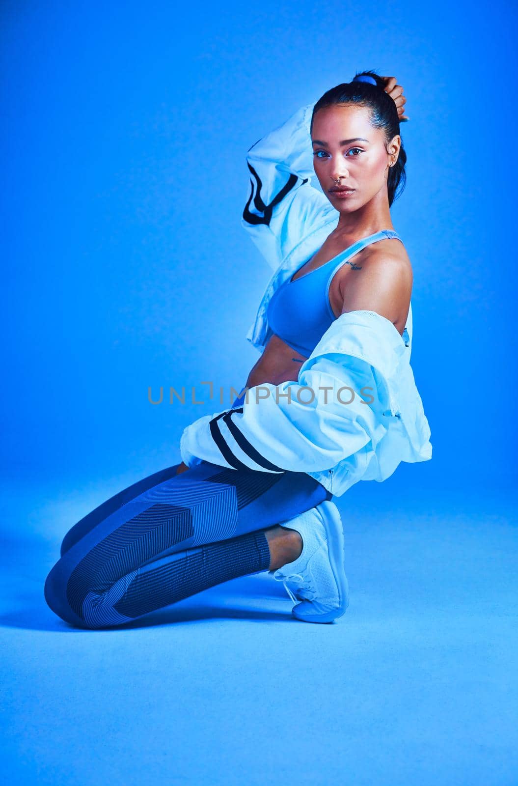 Full length portrait of an attractive young female athlete posing on her knees against a blue background.