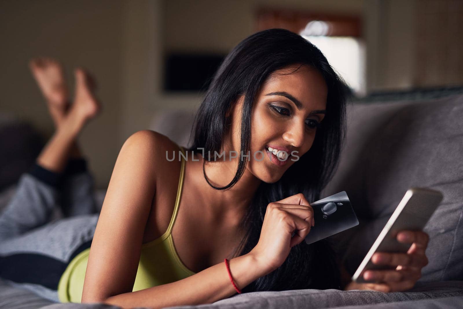 Shot of an attractive young woman shopping online while lying on her sofa at home.