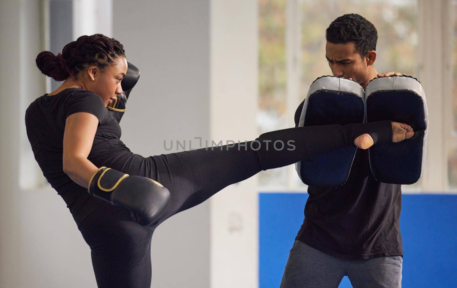 Kickboxing is the best form of dynamic exercise. Shot of a young woman practicing kickboxing with her trainer in a gym. by YuriArcurs