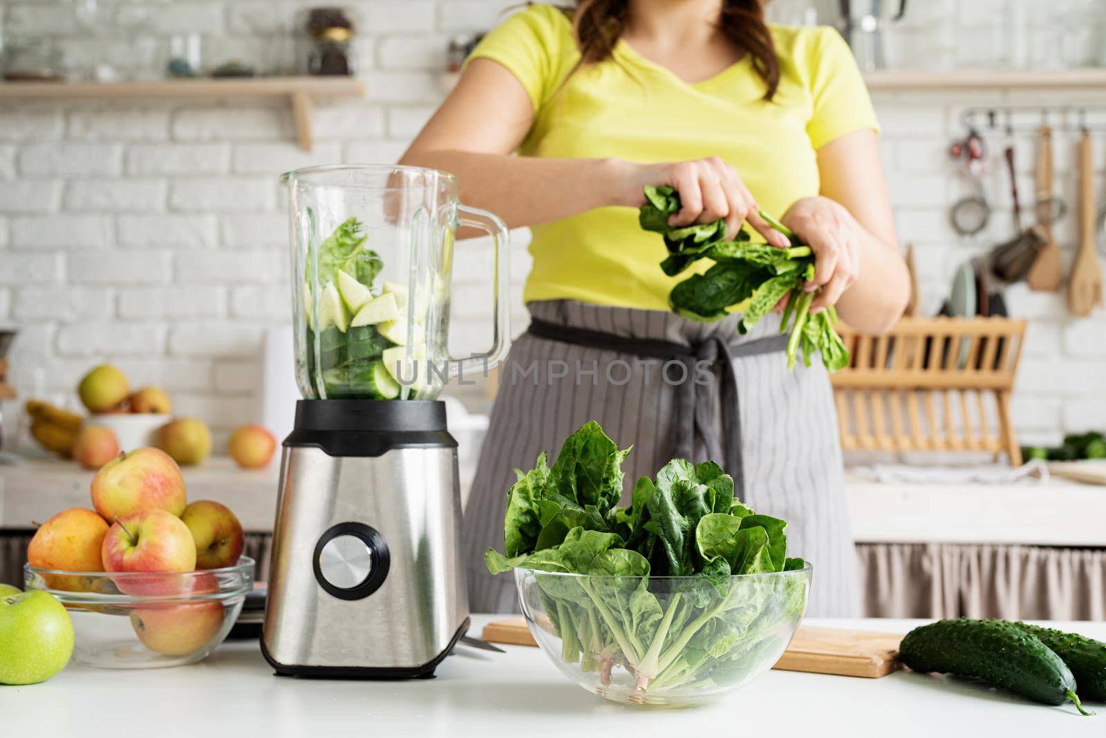 Young woman making green spinach smoothie at home kitchen by Desperada