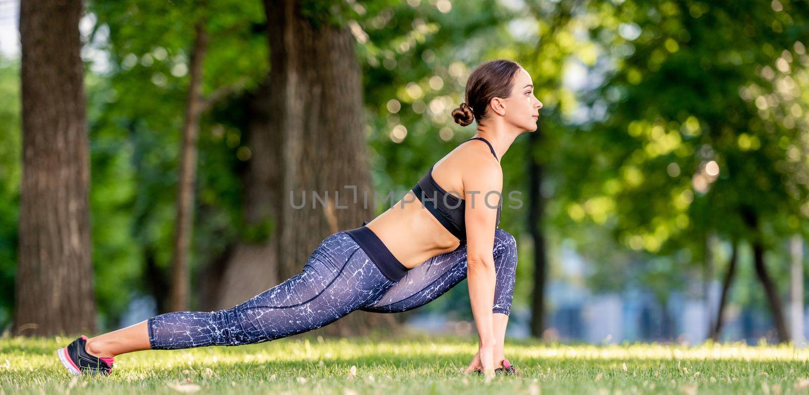 Pretty girl during yoga morning workout at the nature standing in pose in park. Sport woman exercising and stretching her legs outdoors