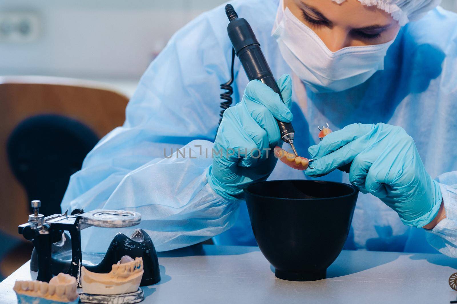 A dental technician in protective clothing is working on a prosthetic tooth in his laboratory by Lobachad