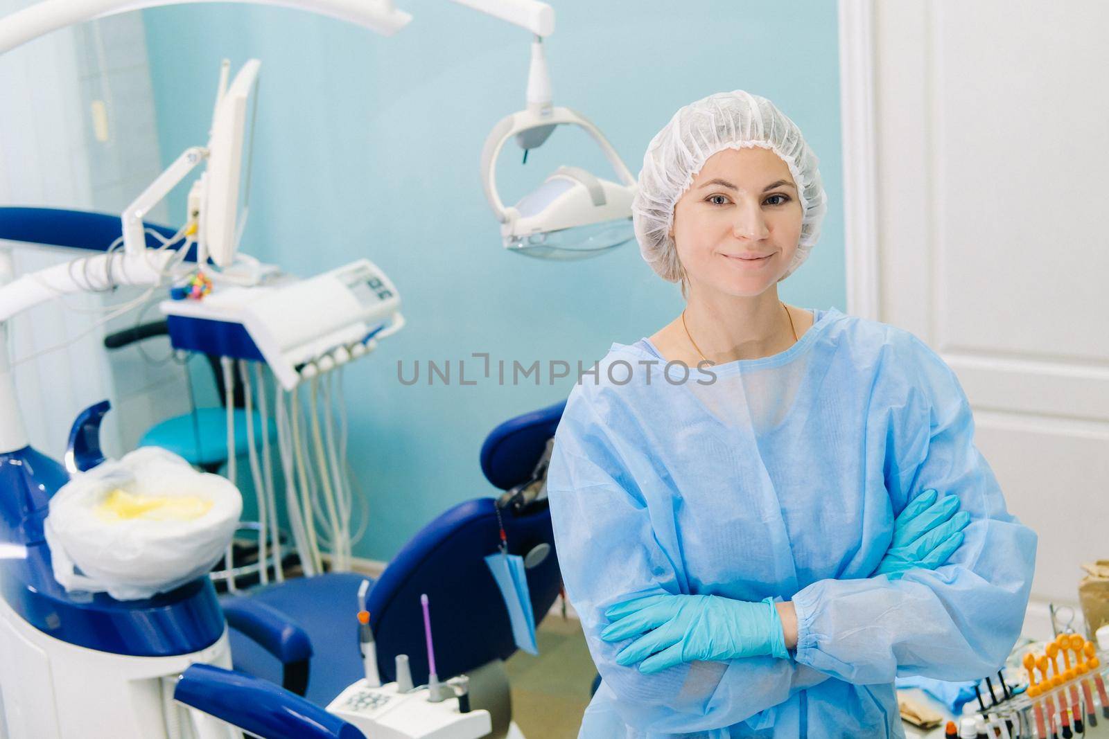 a female dentist poses in front of the camera and folds her arms on her chest in her office by Lobachad