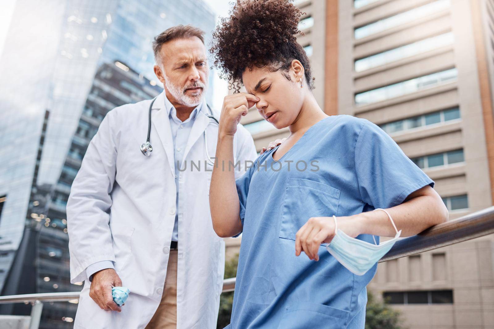 Shot of a young female nurse suffering from a headache while talking to a colleague in the city.