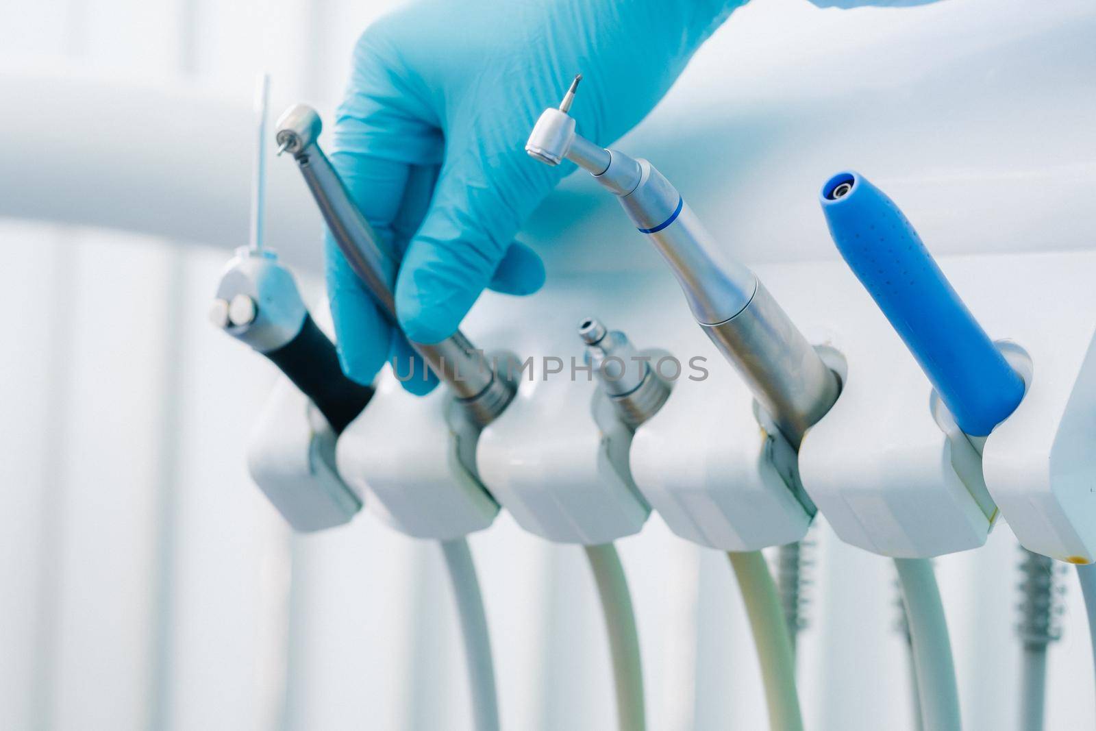 a dentist wearing gloves in the dental office holds a tool before working by Lobachad