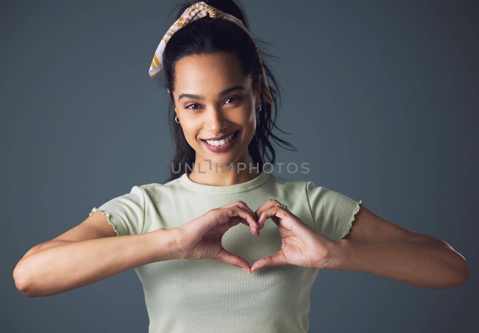 Studio shot of a young woman forming a heart shape while standing against a grey background.