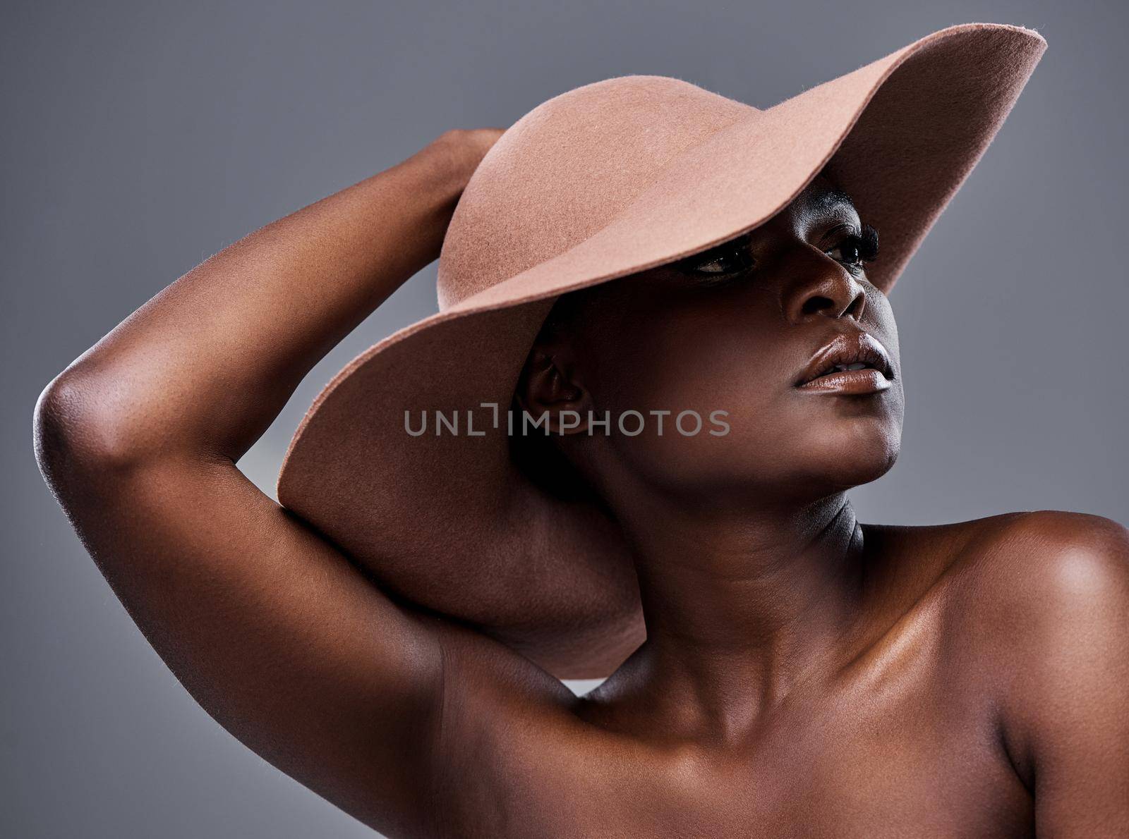 We all glow differently. Shot of a beautiful young woman wearing a hat while posing against a brown background. by YuriArcurs