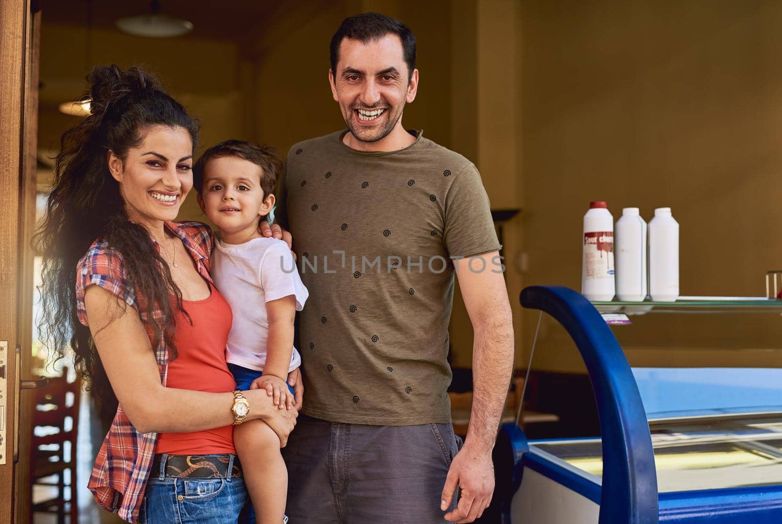 This ice cream shop will be his one day. Cropped portrait of an affectionate family of three standing in the entrance way to their ice cream shop. by YuriArcurs