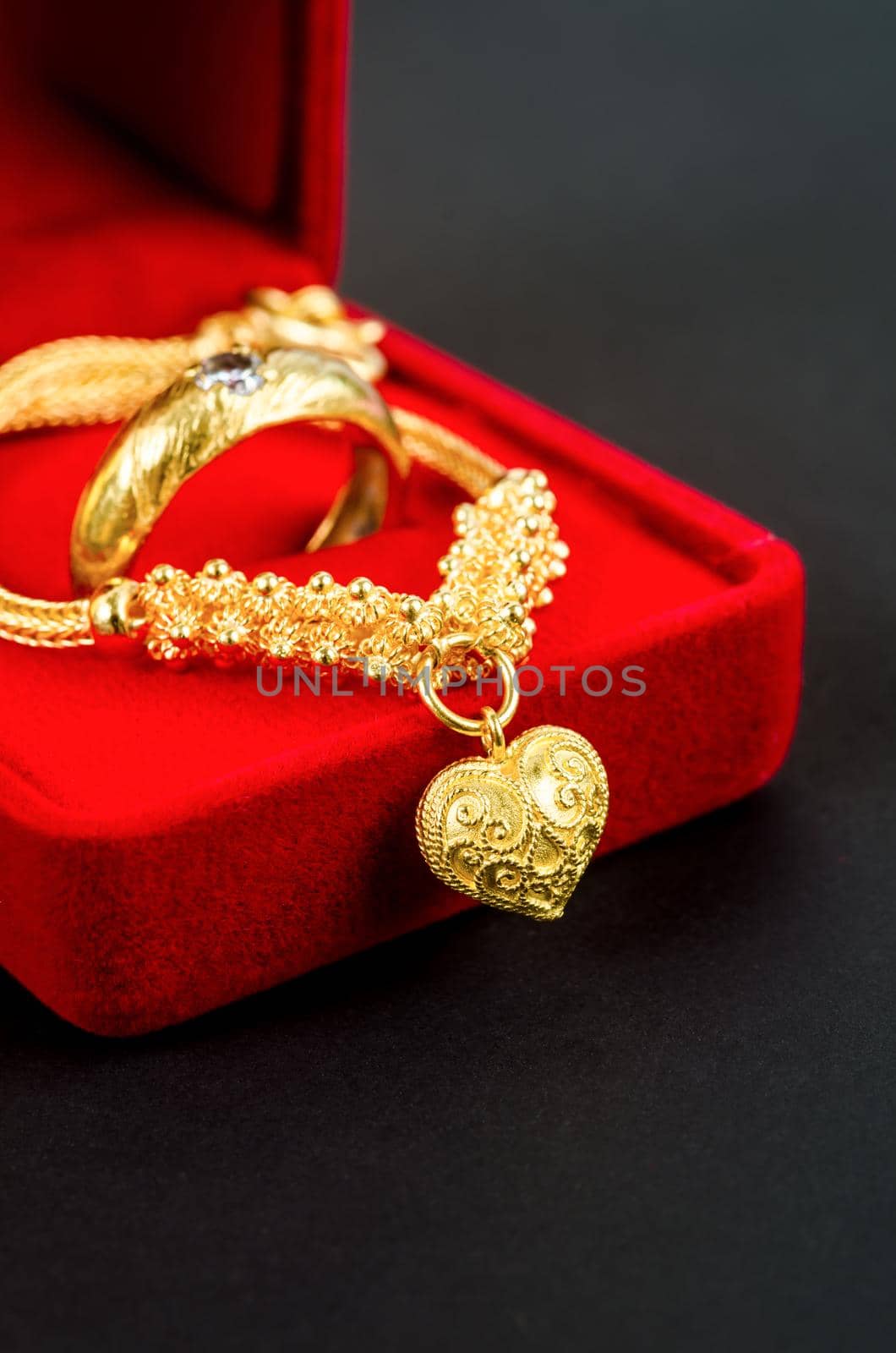 Gold necklace and heart shape pendant and gold ring in red velvet box on black. by Gamjai