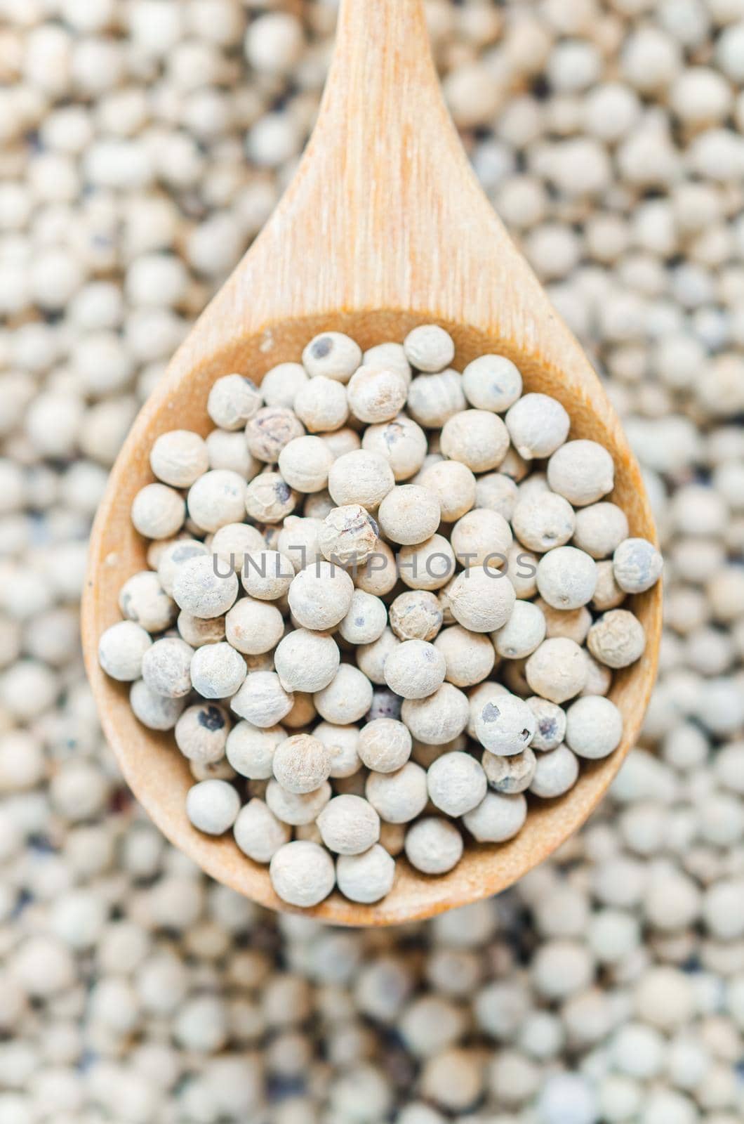 The White pepper seeds (peppercorn) in wooden spoon on tablecloth background.