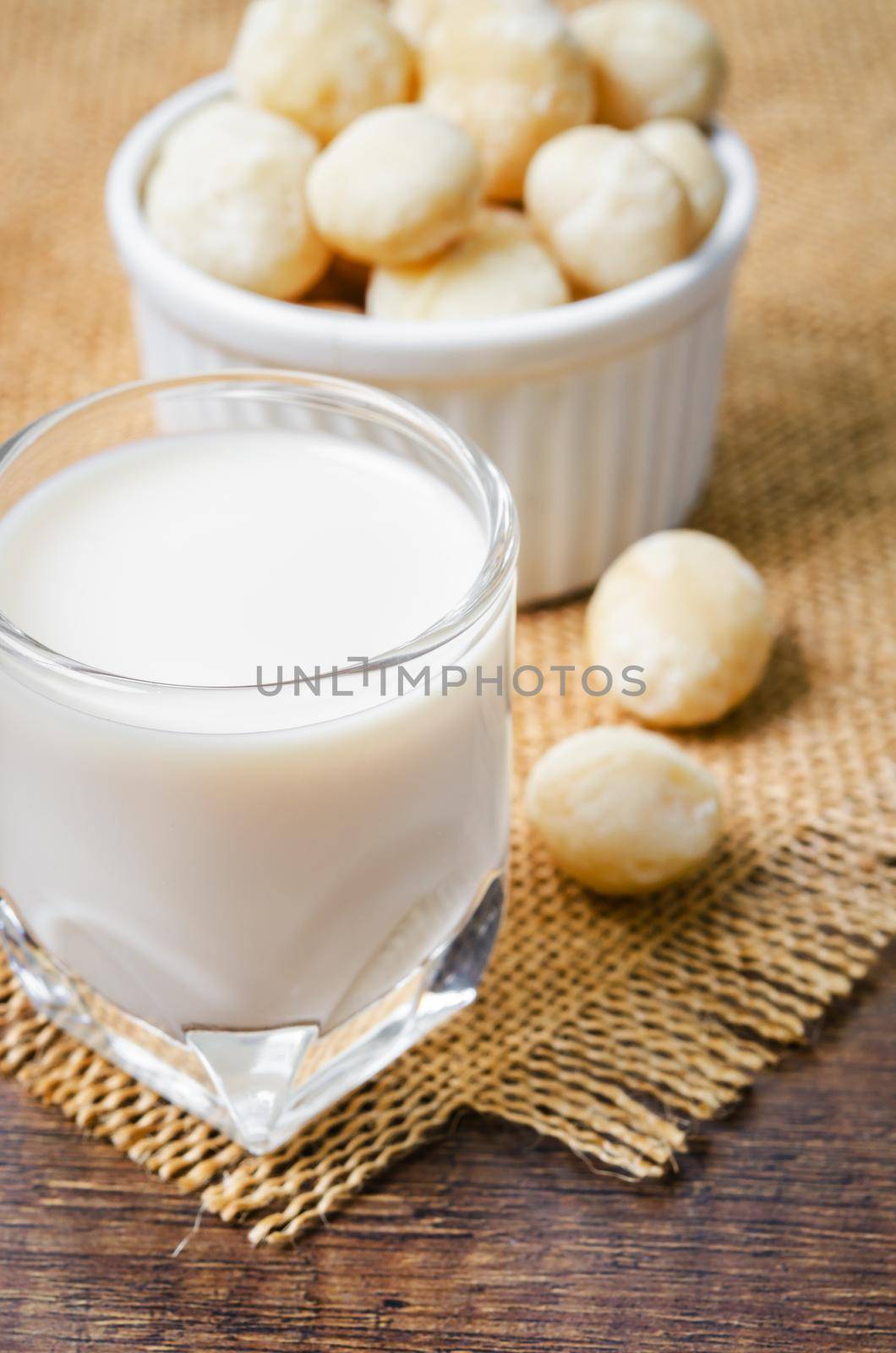 The Macadamia milk in a glass and a bowl of macadamia nuts on a wooden background.