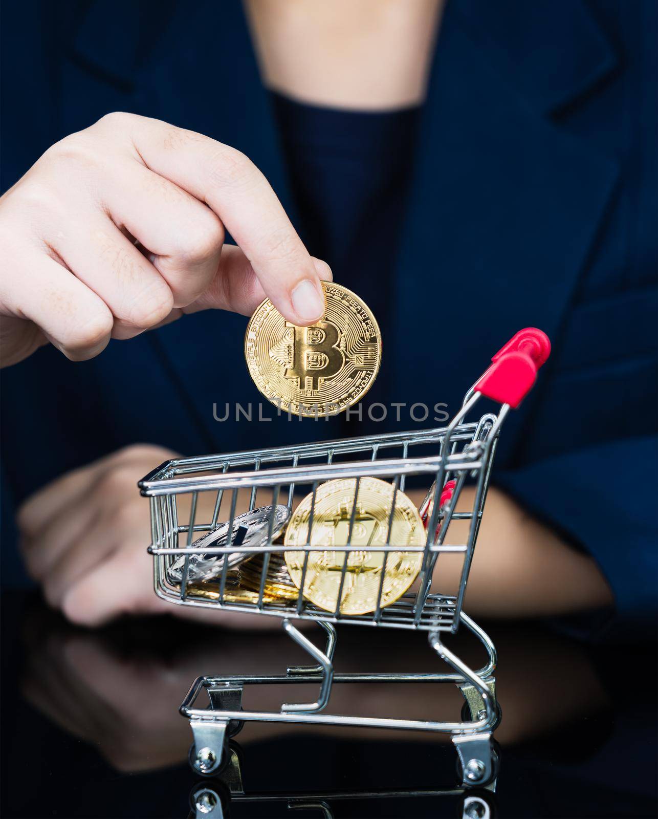 Woman holding some pieces of golden Bitcoin token in shopping cart by stoonn