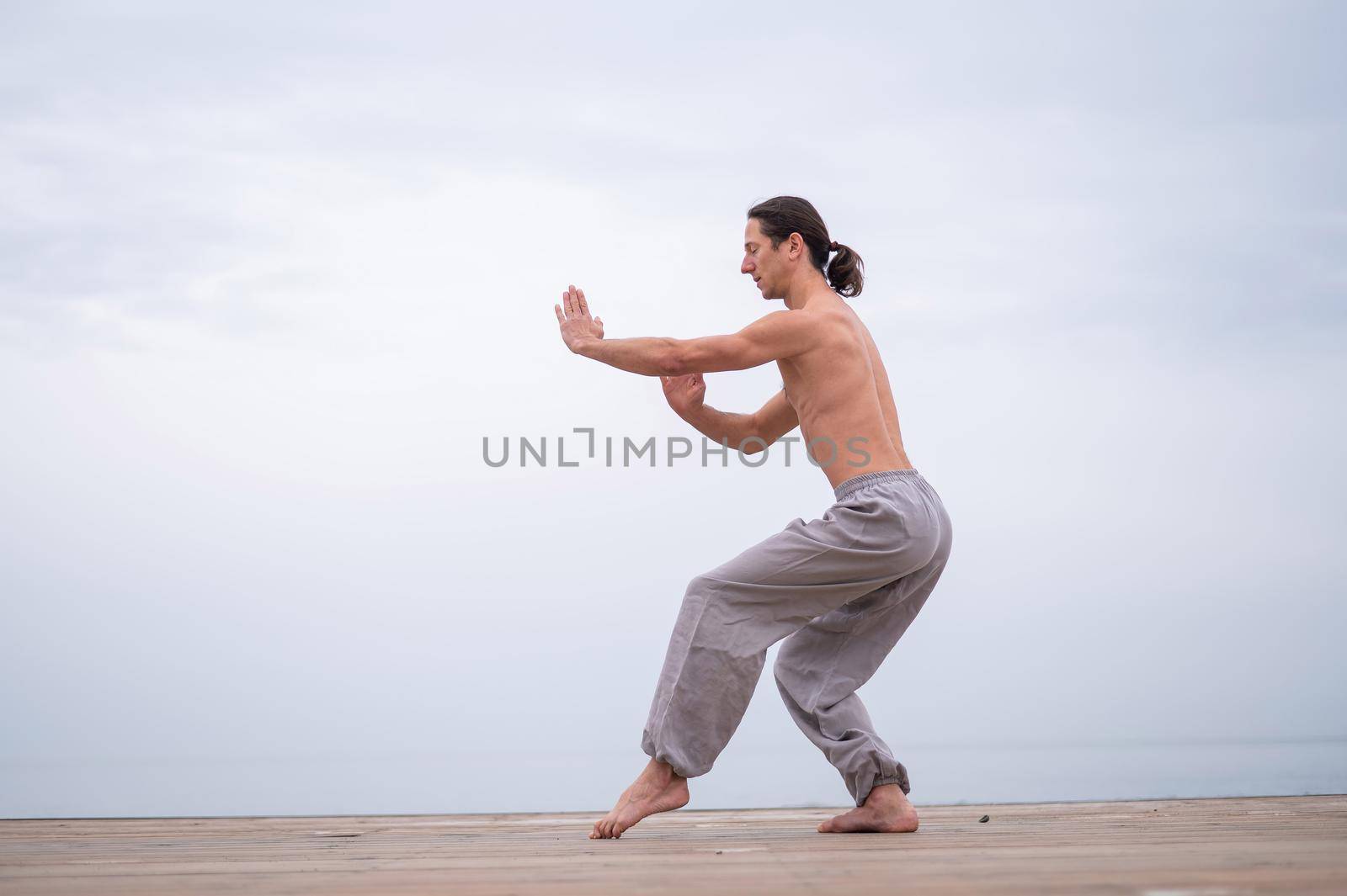 Caucasian man with naked torso practicing wushu on the seashore