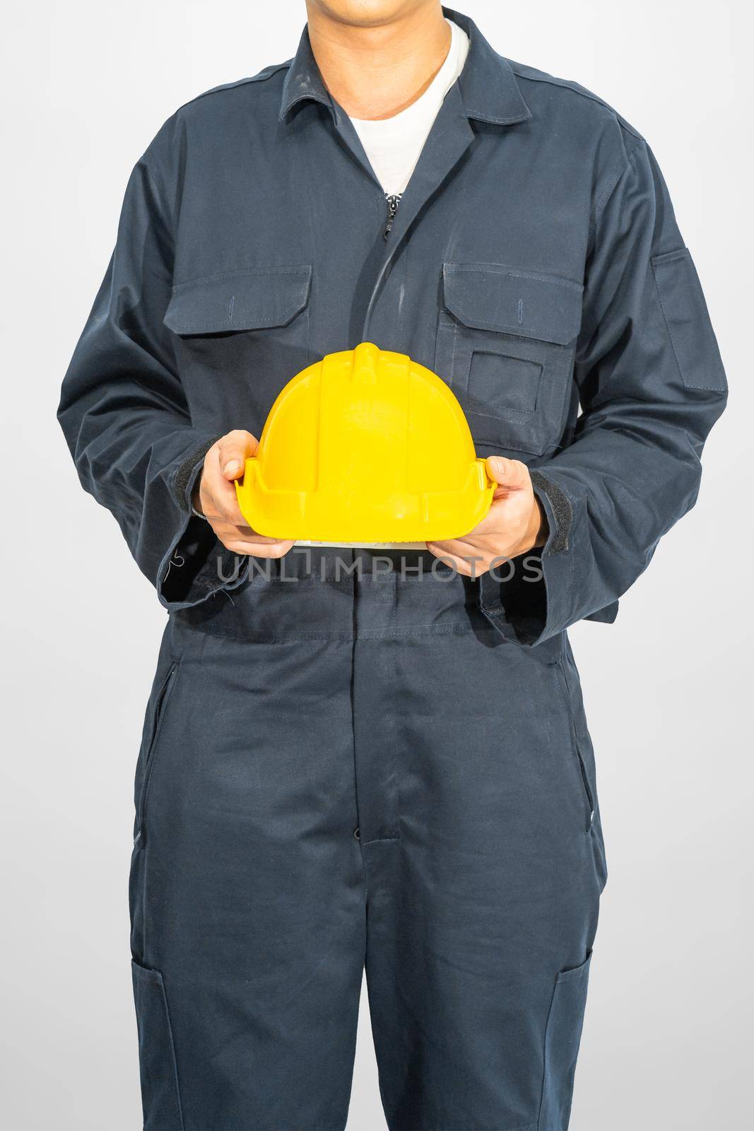 Worker standing in blue coverall holding yellow hardhat isolated on gray background