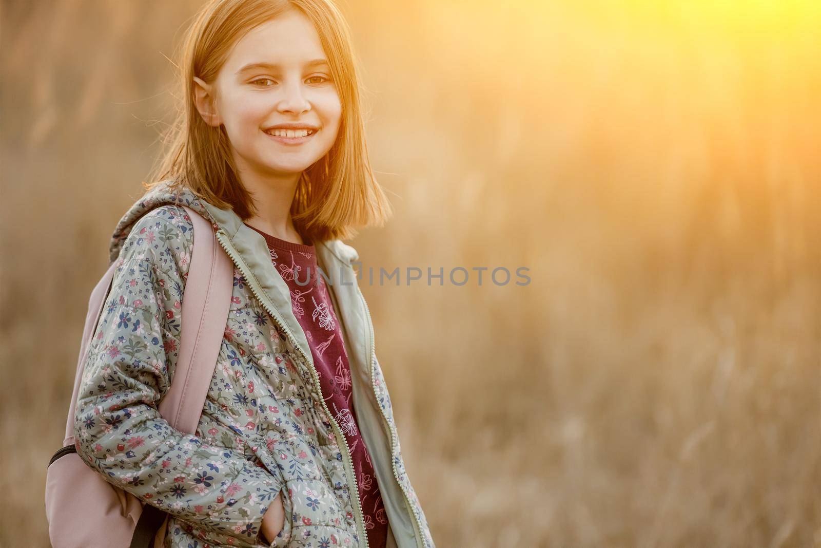 Preteen girl child looking at camera and smiling in amazing sunset light in the field. Beautiful portrait of pretty female kid