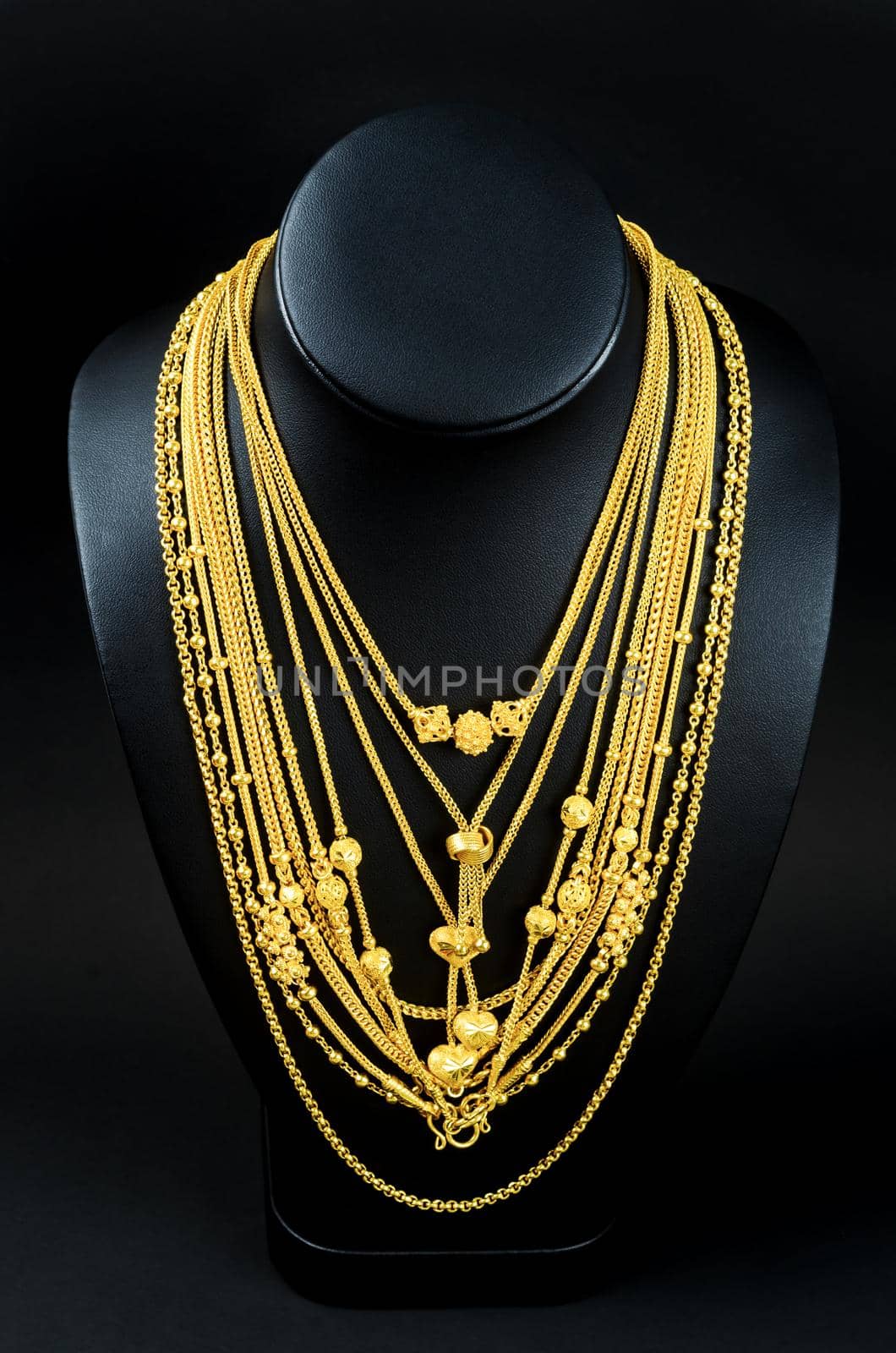 Necklace display stand with gold necklace on black background. by Gamjai