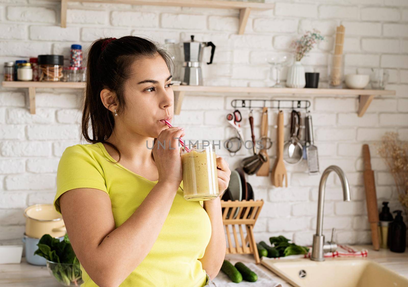 Healthy eating, dieting concept. Young brunette woman drinking fruit banana smoothie at home kitchen from mason jar