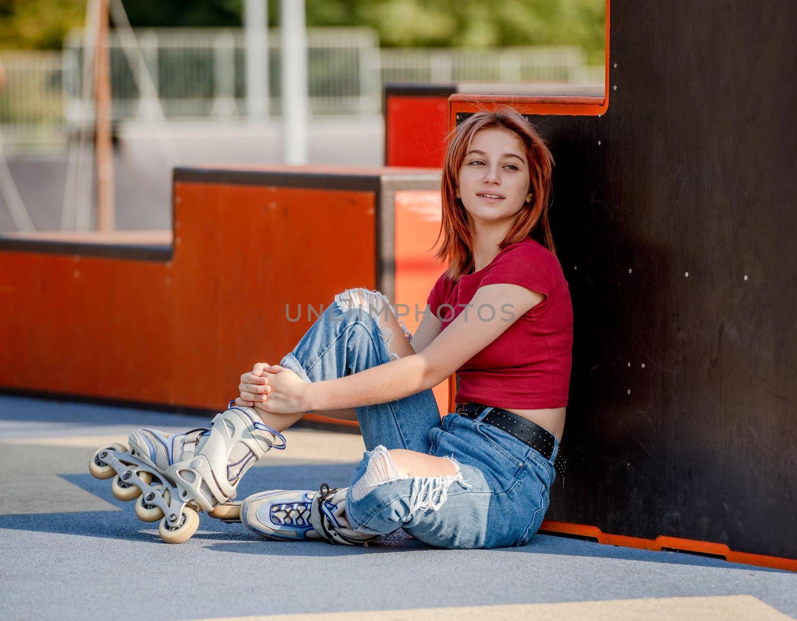 Beautiful girl wearing roller skates sitting on ground and looking back. Pretty female teenager skater portrait