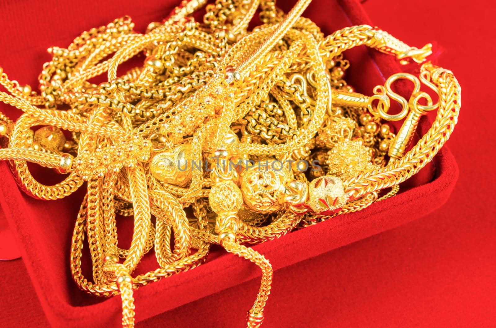 The many gold necklaces in a red velvet box on red background.
