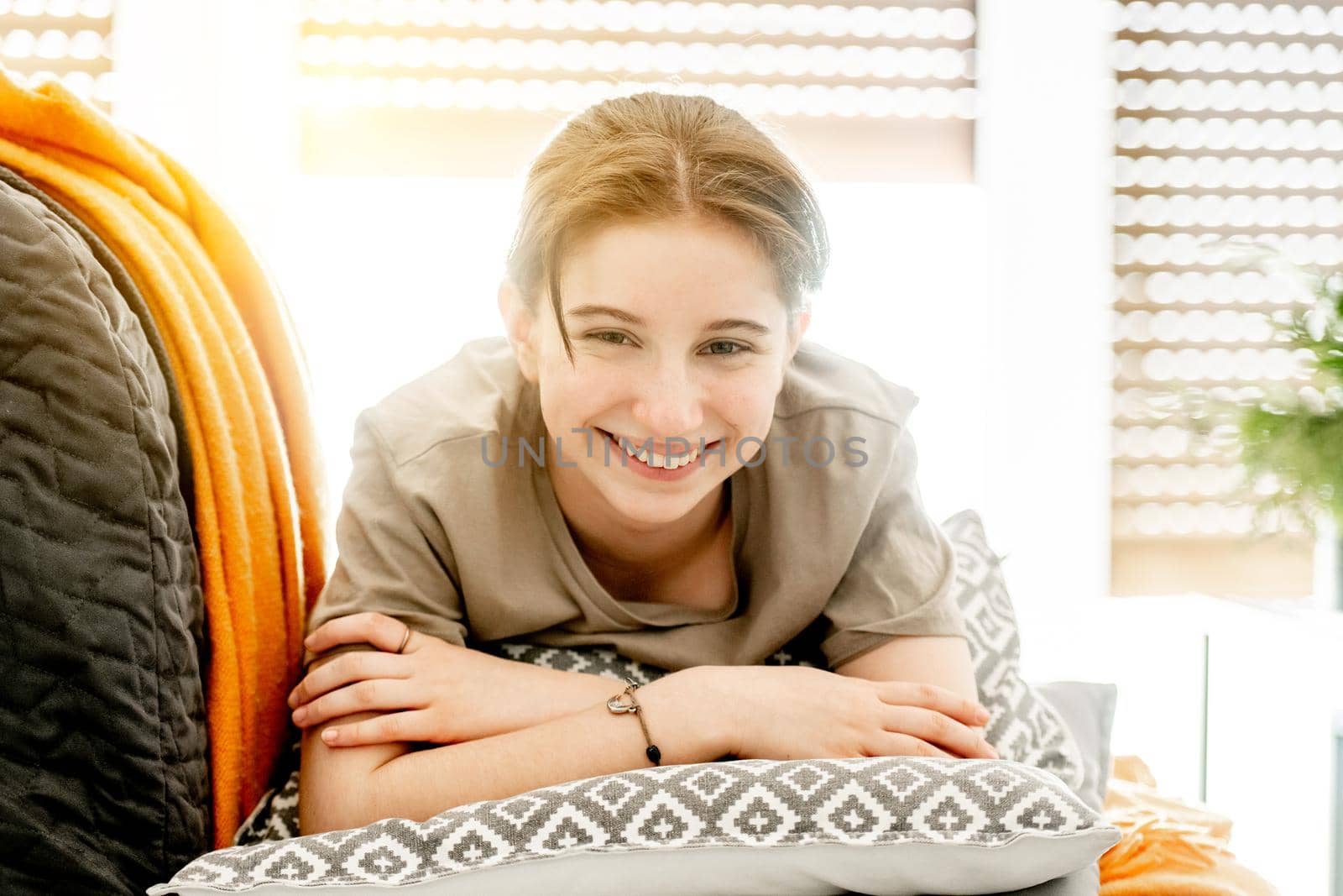 Smiling girl lies on pillow on sofa at home. Female teenager resting on couch in light room