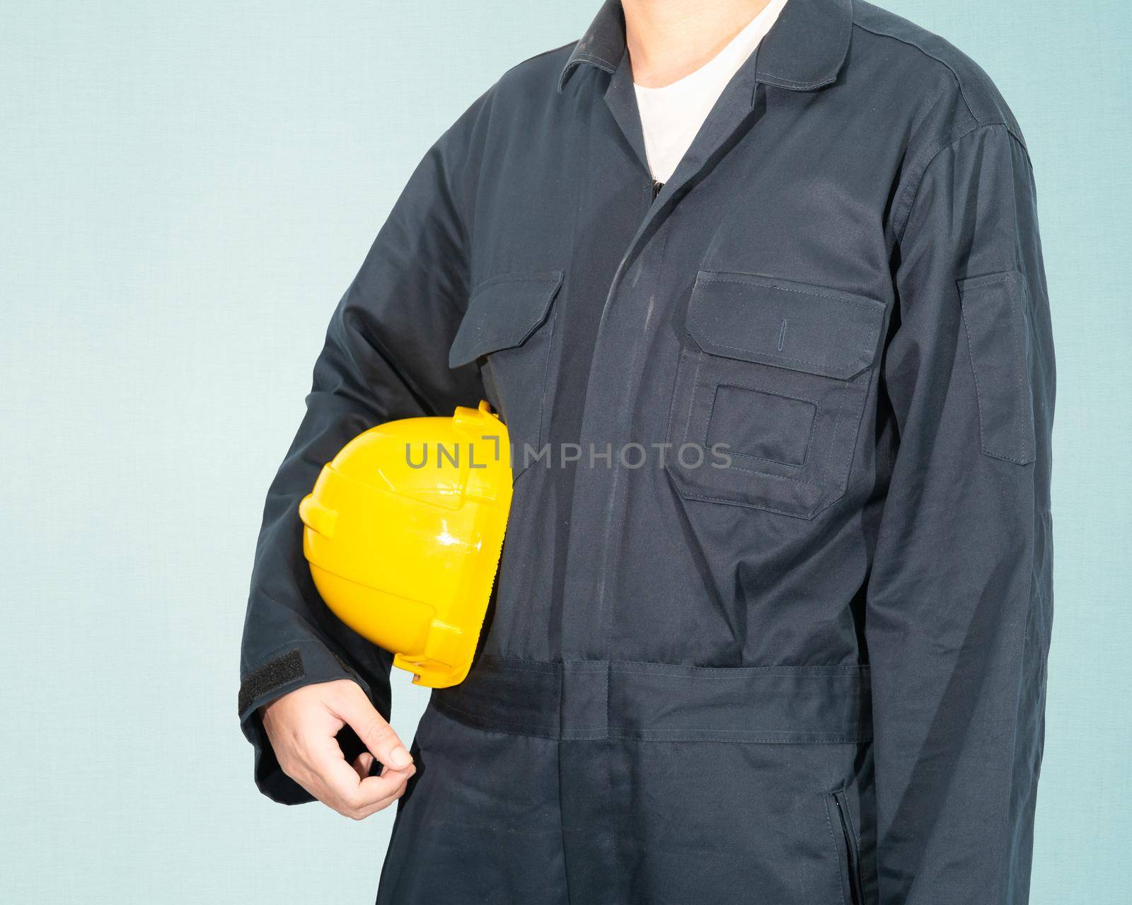 Worker standing in blue coverall holding yellow hardhat by stoonn