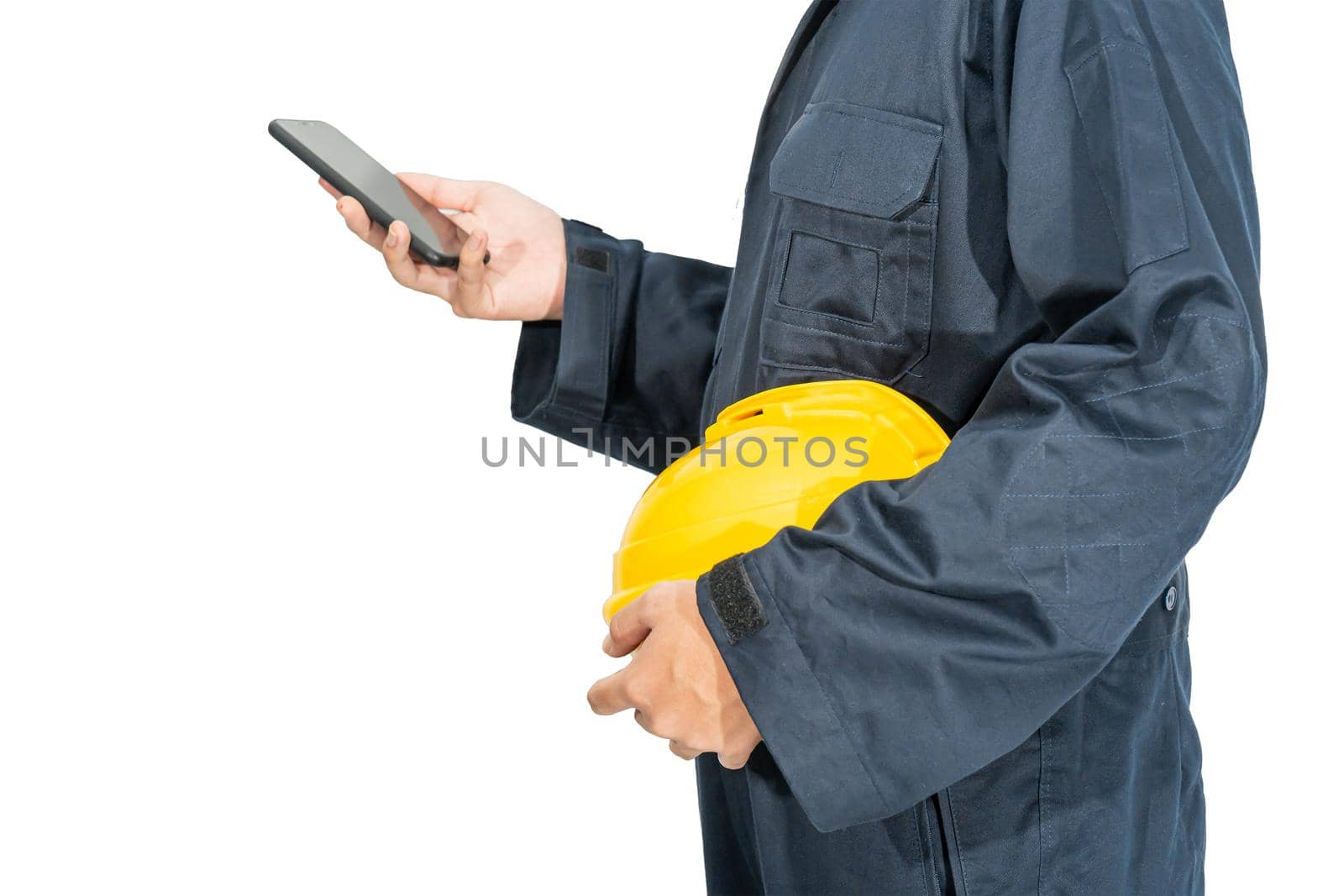 Worker standing in blue coverall holding hardhat and use smartphone by stoonn