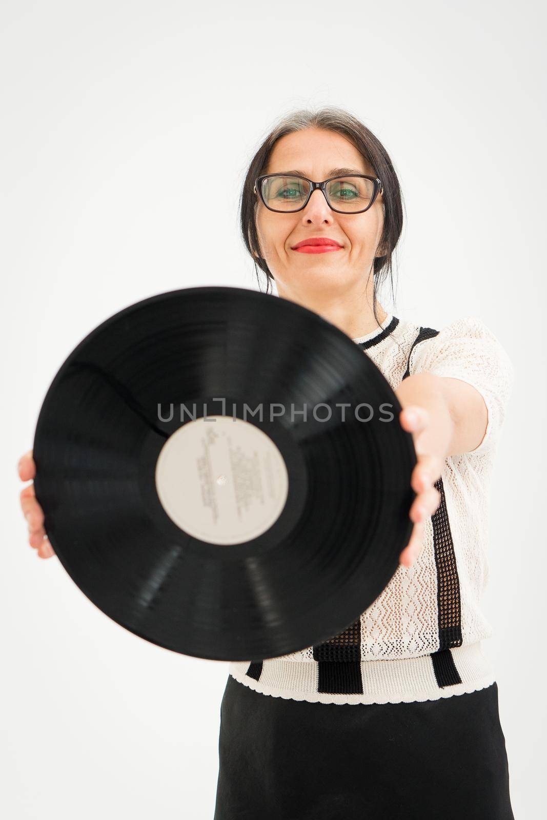 Studio photo of middle aged woman starting getting grey-haired wearing black and white clothes with vinyl record in hands on white background, middle age sexy lady, happy life concept by balinska_lv
