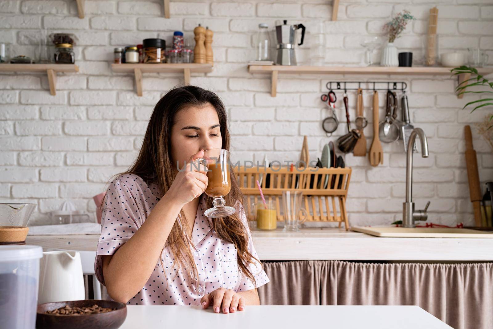 young woman in lovely pajamas drinking coffee at home kitchen by Desperada