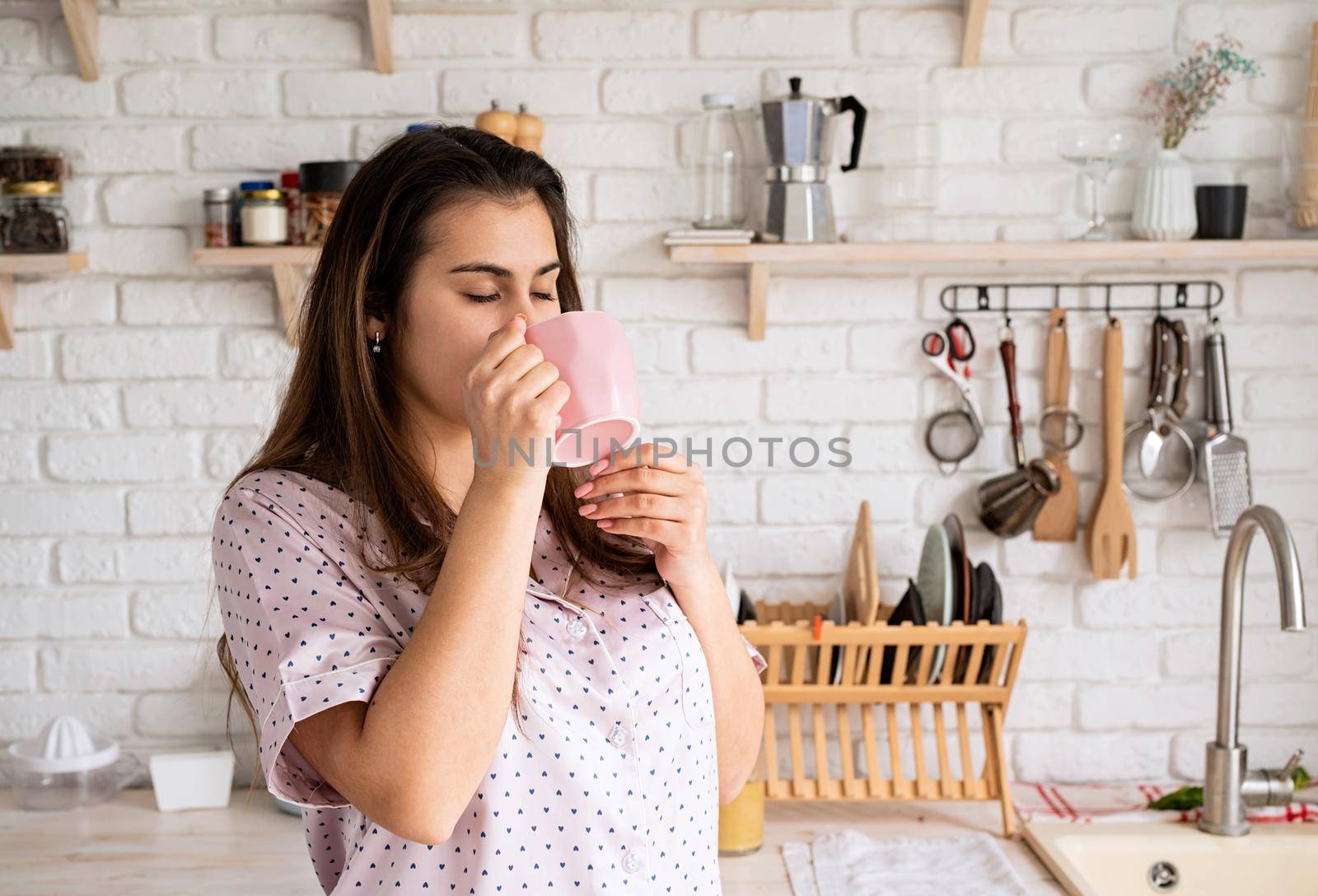 young woman in lovely pajamas drinking coffee at home kitchen by Desperada