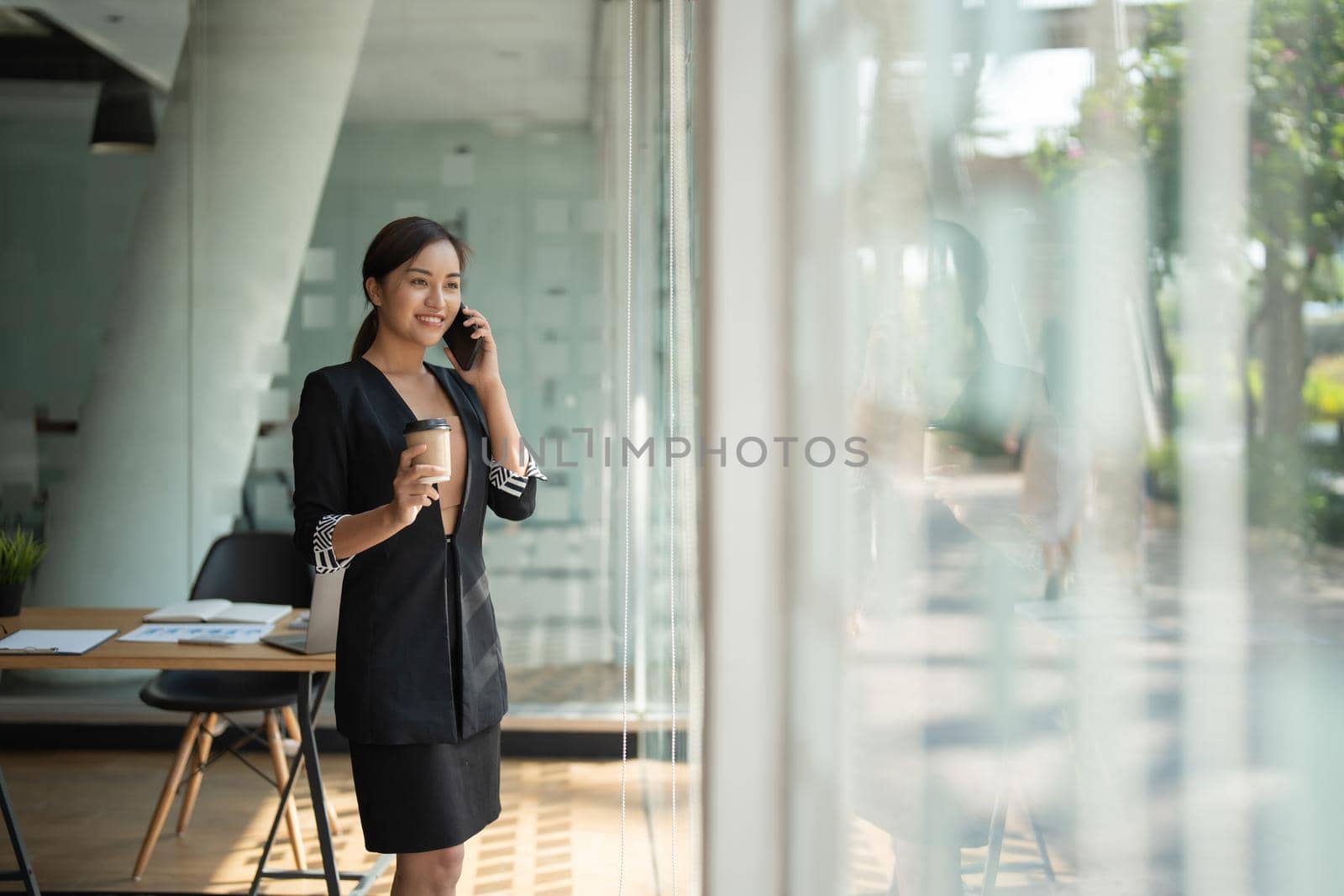 Asian business woman making a phone call and smiling at modern office.