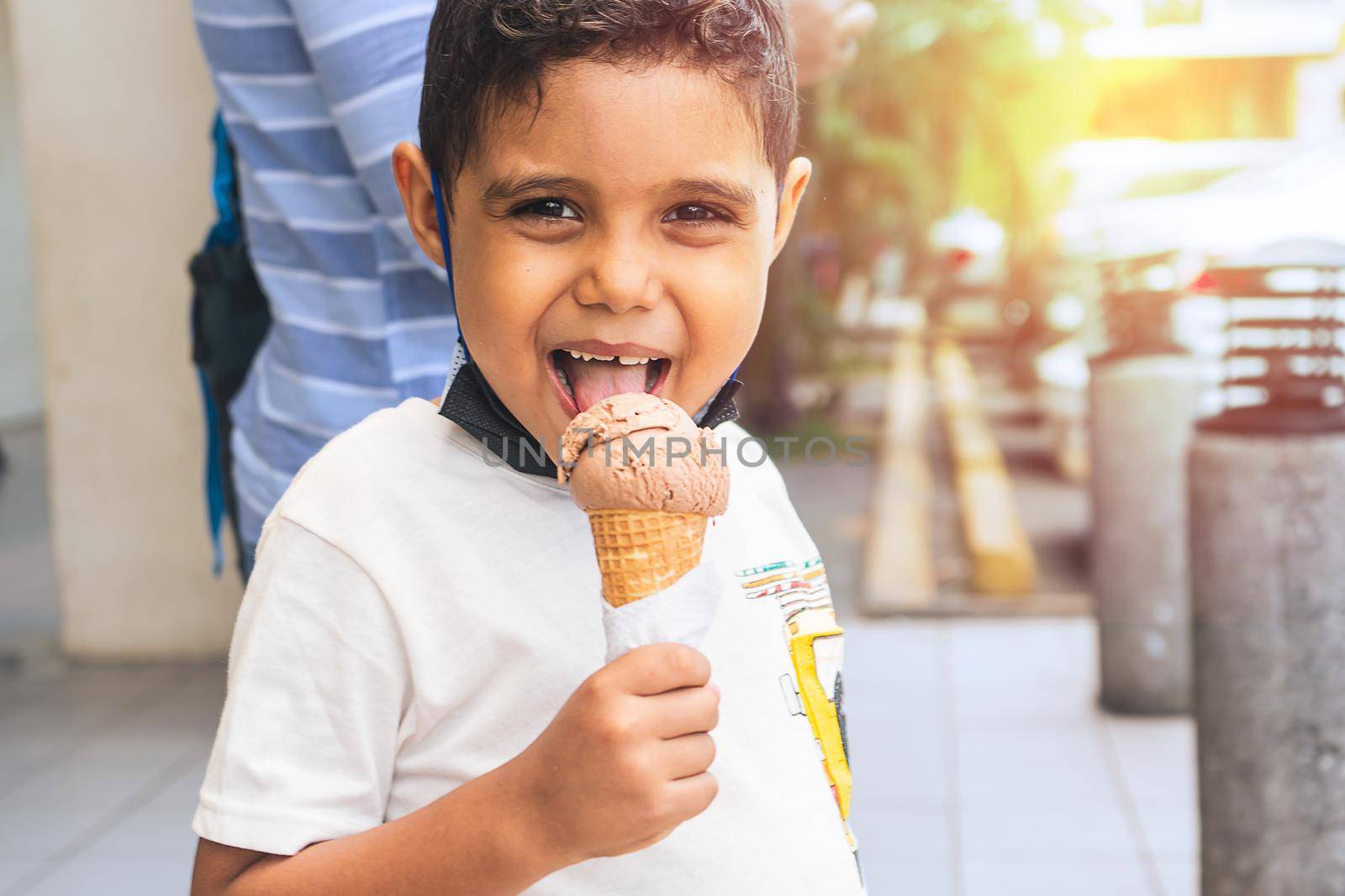 Latin boy with mischievous face enjoying an ice cream during the summer break in a shopping center by cfalvarez