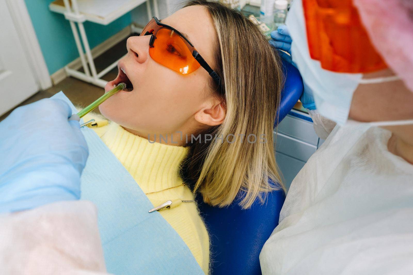 A young beautiful girl in dental glasses treats her teeth at the dentist with ultraviolet light. filling of teeth by Lobachad