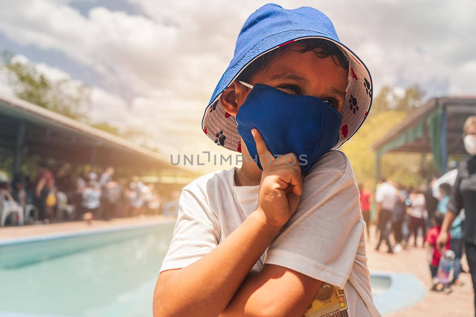 Latin boy enjoying summer in a pool very happy dressed in comfortable clothes and a bucket hat and mask