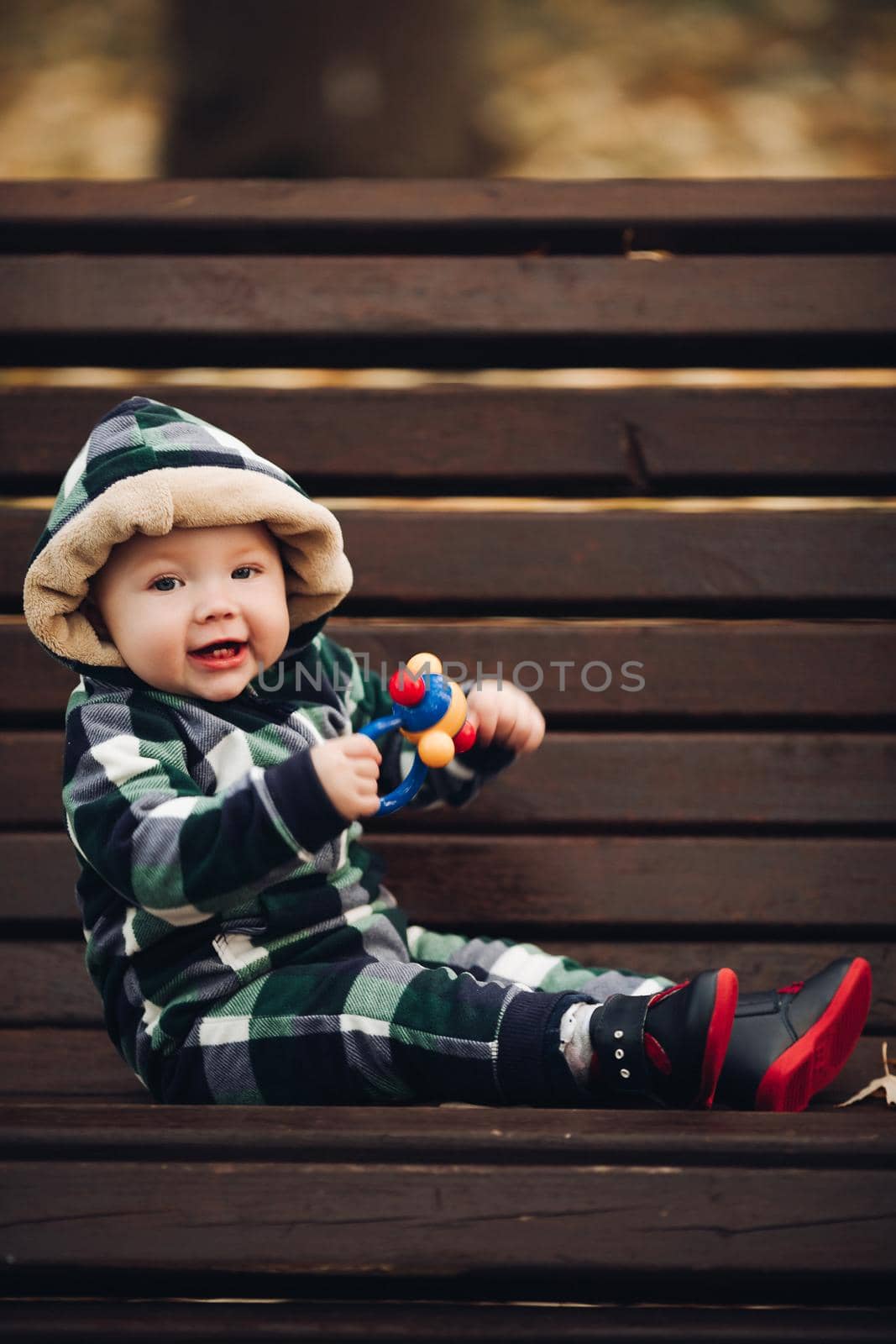 Adorable baby in warm overall with hood sitting on foliage. by StudioLucky