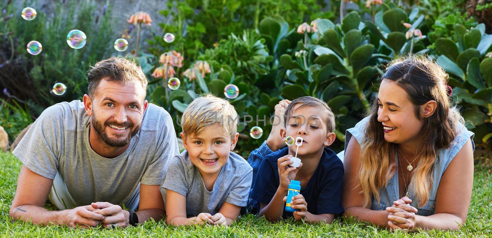 Portrait of a beautiful family laying on the grass and playing with bubbles in a backyard.