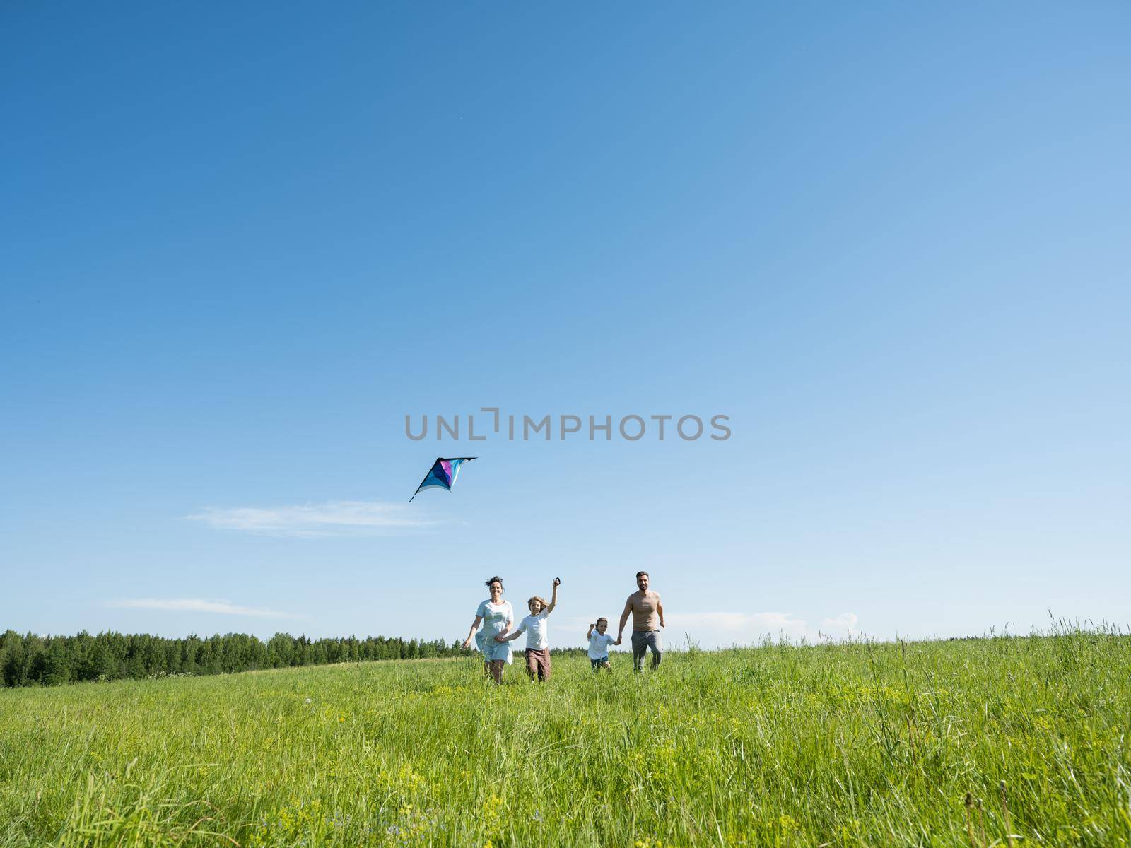 Family of parents and children running through field letting kite fly