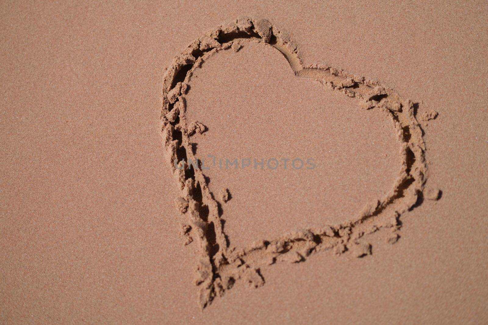 Heart is painted on sand of sea beach closeup. Honeymoon romantic trip concept