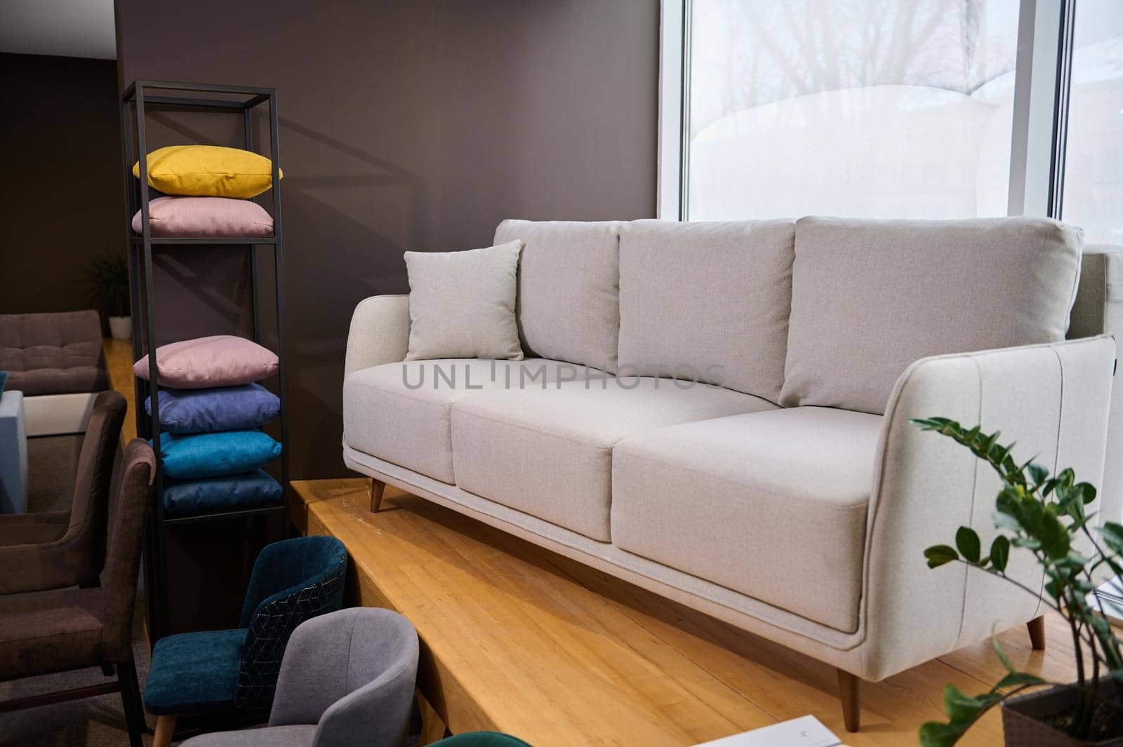 Stylish minimalist white settee with pillows displayed for sale in a showroom of modern furniture, next to stand with colorful cushions from fabrics of different texture, softness, colors and quality by artgf